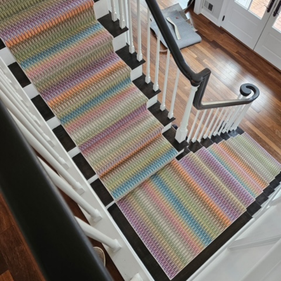 A staircase with a colorful, striped runner carpet on black risers and white banisters.